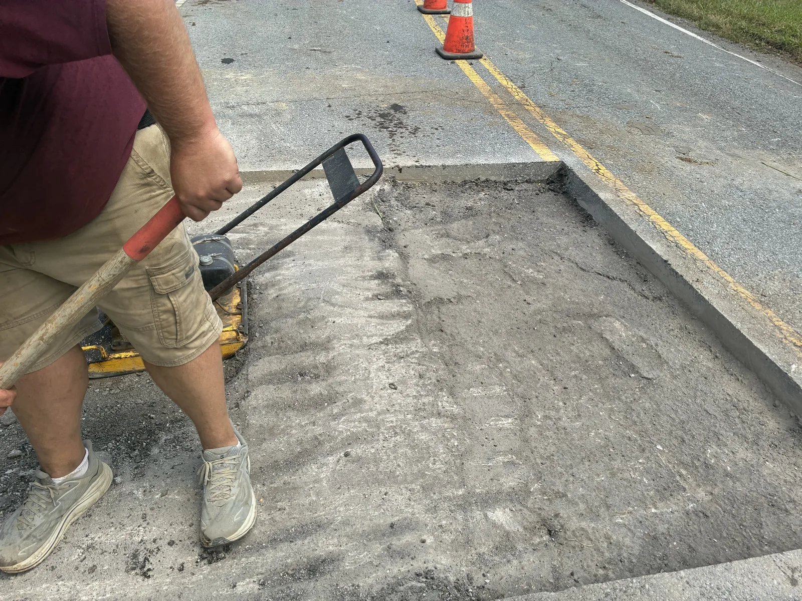 Plate compactor packing the base of a road cut over a sewer line crossing