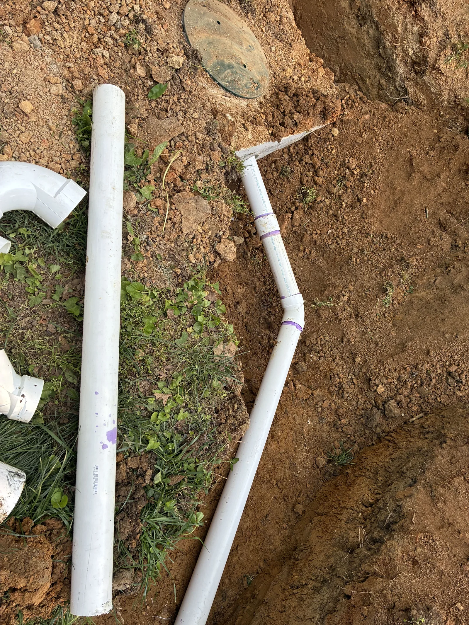 Round septic tank lid at grade beside new pipe in the trench